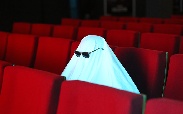 A person dressed as a ghosts sitting in a movie theater. 