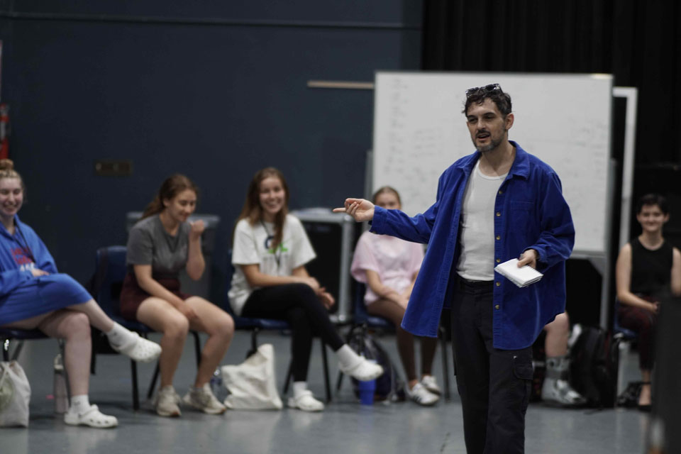 A man wearing a blue jacket speaks to an engaged audience, sharing insights during a group discussion.