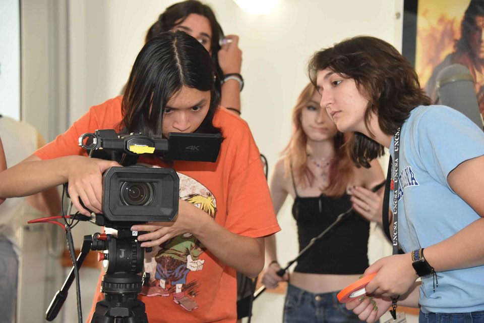 Several individuals standing together around a video camera, engaged in conversation and planning for a shoot.