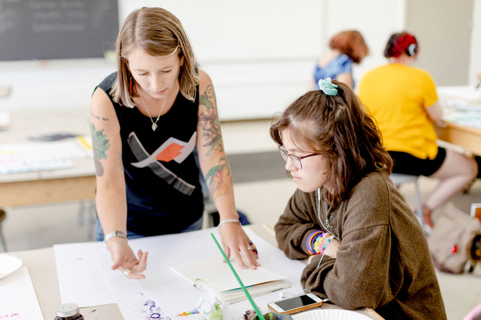 A woman and a girl collaborate on a project together in a classroom setting.